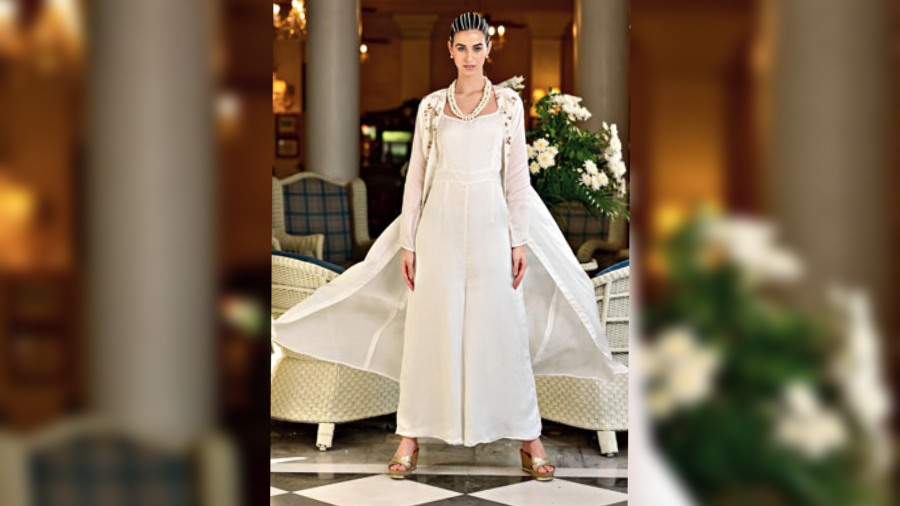 A smart occasionwear or brunch style, the white jumpsuit with semi-flared bottom is paired with an organza jacket detailed with resham thread embroidery and sequins