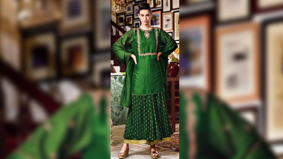 Take the glam quotient a notch higher this wedding season in this vibrant bottle-green silk kurta. It is designed with intricate floral zardozi work on the neckline and yoke in carmine and gold and extends on the sleeves with buta design. The look is completed with a Benarasi sharara
