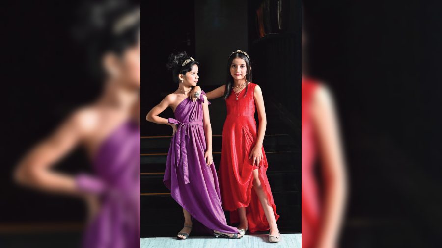 Aditri and Kaira cut a beautiful frame together in their solid-colour crepe and raw silk outfits. Aditri sports a draped toga dress in purple and Kaira dons an asymmetric red draped gown designed with scalloped edging along the hemline. Their looks are accessorised with black velvet hairbands detailed with metal embellishments.