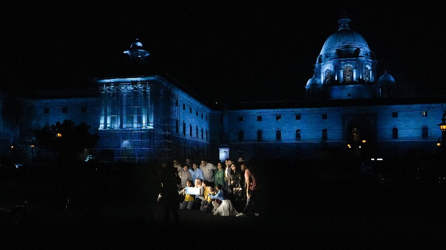 Children pose for photographs in the backdrop of North Block illuminated in New Delhi. 