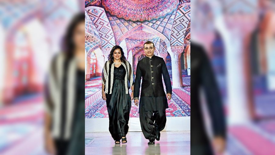 Rajeev Agarwal paired a black asymmetrical kurta and cowl salwar with a black bundi highlighted with gold sequins. Saroj Agarwal walked in a black draped outfit teamed with a resham-embroidered sheer cape