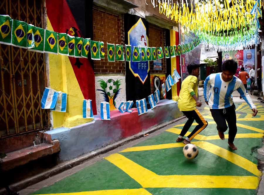 Young boys play football wearing jerseys of Argentina and Brazil in a street decorated with flags of the teams and other Football World Cup-themed graffitis on Monday