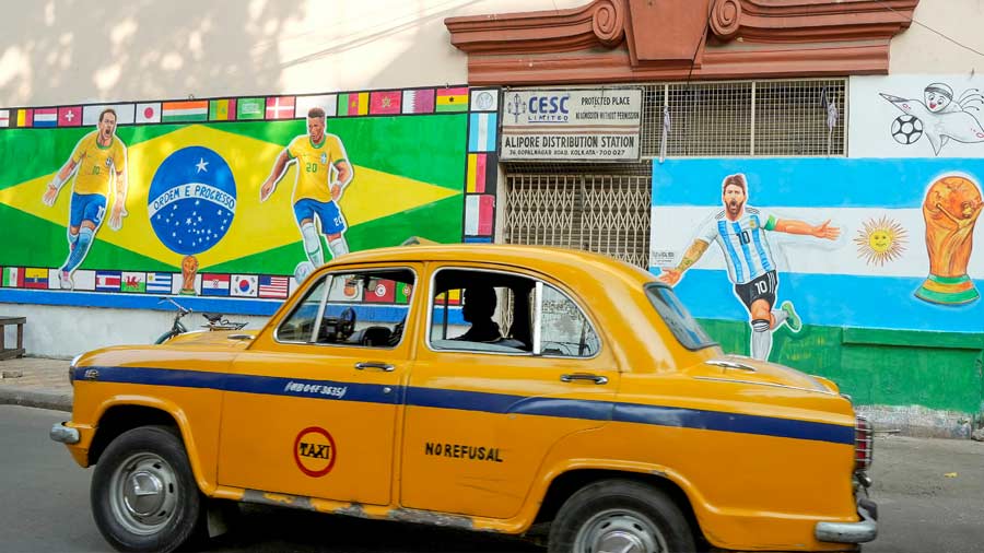 A taxi moves past a wall depicting a mural of Brazilian and Argentinian players for ongoing FIFA World Cup.