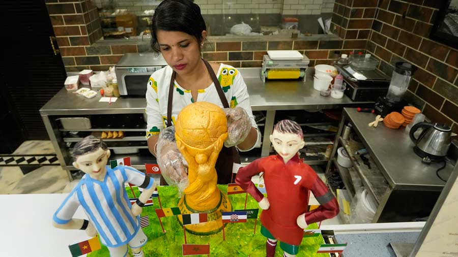 A confectionery shop employee prepares a cake featuring a replica of the FIFA World Cup 2022 trophy and celebrated footballers Lionel Messi and Cristiano Ronaldo. 