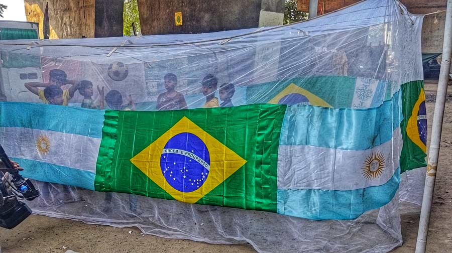 Children play football inside a large mosquito net with flags of Brazil and Argentina, near Hastings