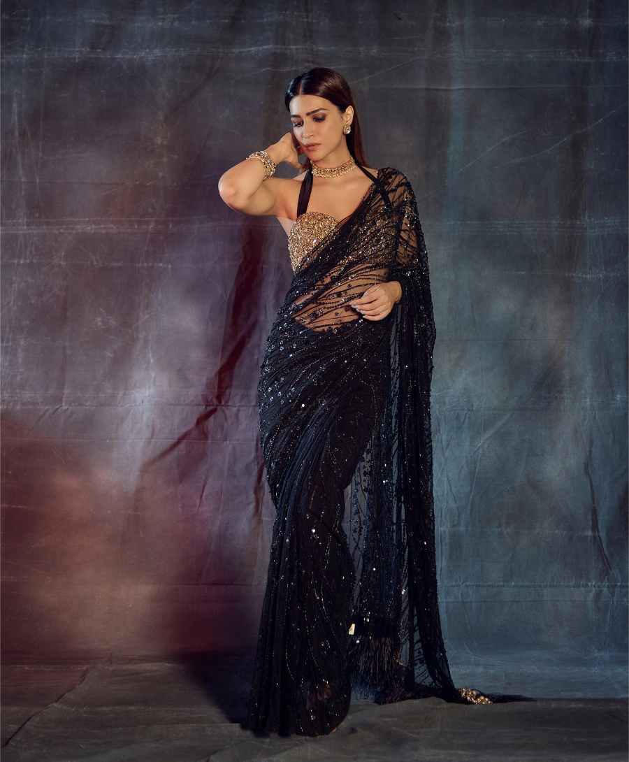 Festive season fashion can be minimalist yet head-turning. Kriti nails it with this black shimmery sheer sari with a halter-neck blingy blouse and matching golden jewellery. 