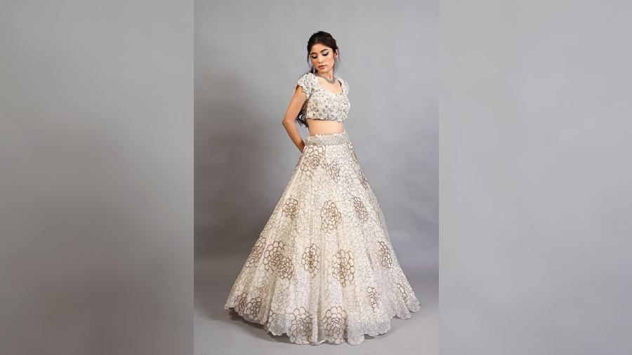 An off-white applique blouse in tulle embellished with organza flowers and mukaish work teamed with a silk organza skirt, with bugle beads, is an apt choice for a subtle bride for one of her wedding functions.
