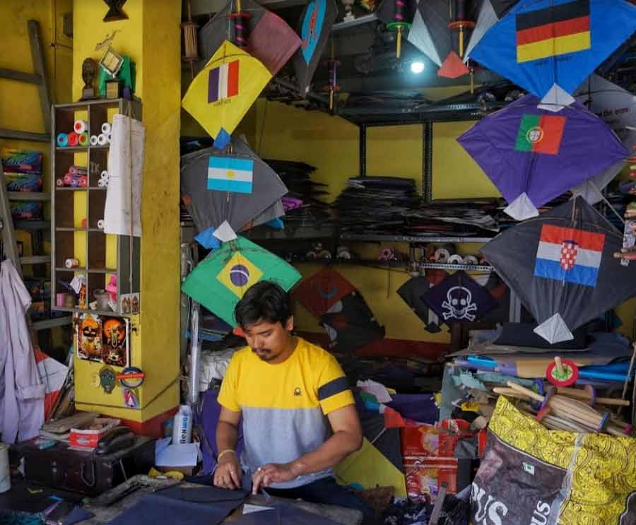 A shop owner is surrounded by kites with flags of different teams competing in the FIFA World Cup 2022 for sale at a kite shop in Santosh Mitra Square on Wednesday
