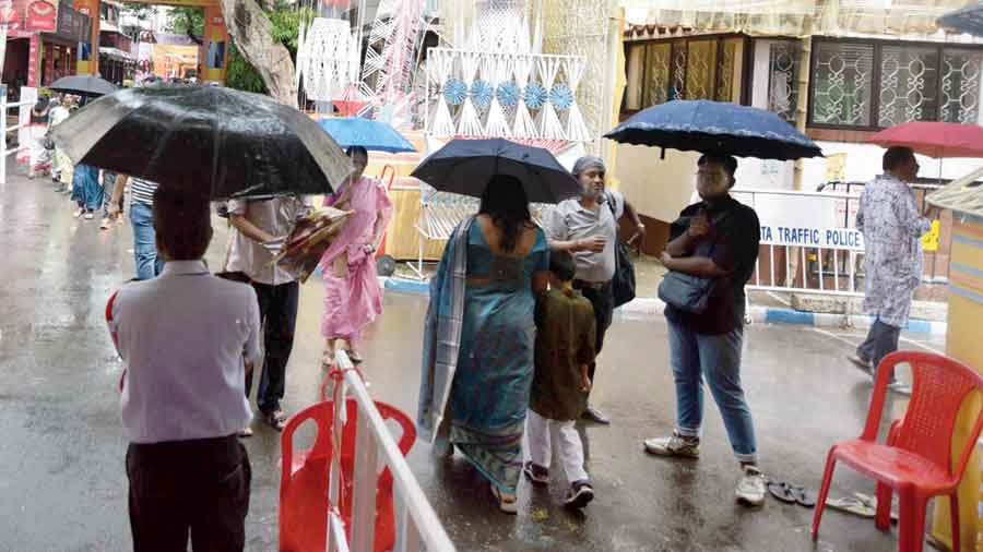 Pandal-hoppers armed with umbrellas visit Mudiali Club in the rain on Monday morning.