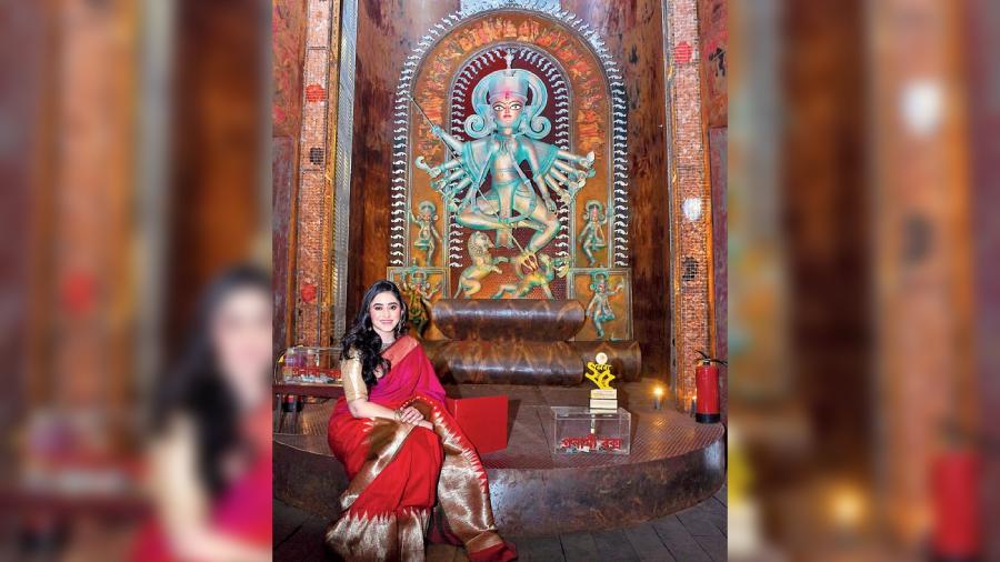 Ridhima Ghosh poses in front of the Goddess in a beautiful metallic red sari, which is adding a more rusty look to the industrial vibe of the pandal.