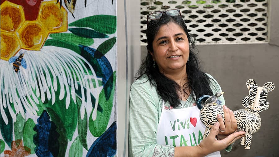 Shukti with her favourite piece, a tiger and a bird in front of a wall painted by her daughter. ‘It’s a reflection of the symbiotic relationship that exists in nature-based mutualism,’ the potter said 