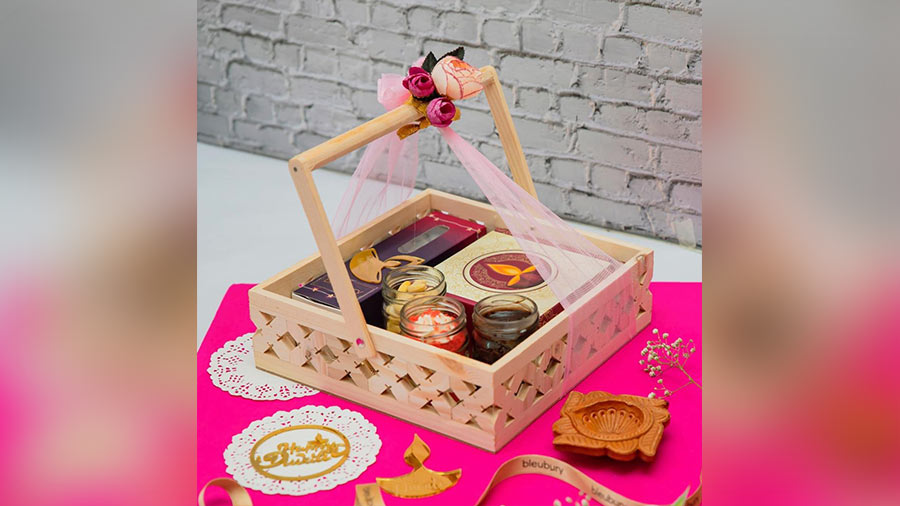LUXE DIWALI HAMPER BASKET FROM BLEUBURY: With a jar of cashew nuts, red velvet cake and chocolate cake jars, cake pops and tea cake slices — this box is a dessert lover's dream. The pinewood basket looks chic and makes for a great gift for friends this season. 