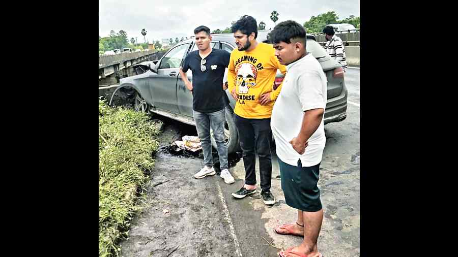 Passers-by gather near the wreckage and look at a person (not in picture) lying motionless among the shrubs near the accident site.