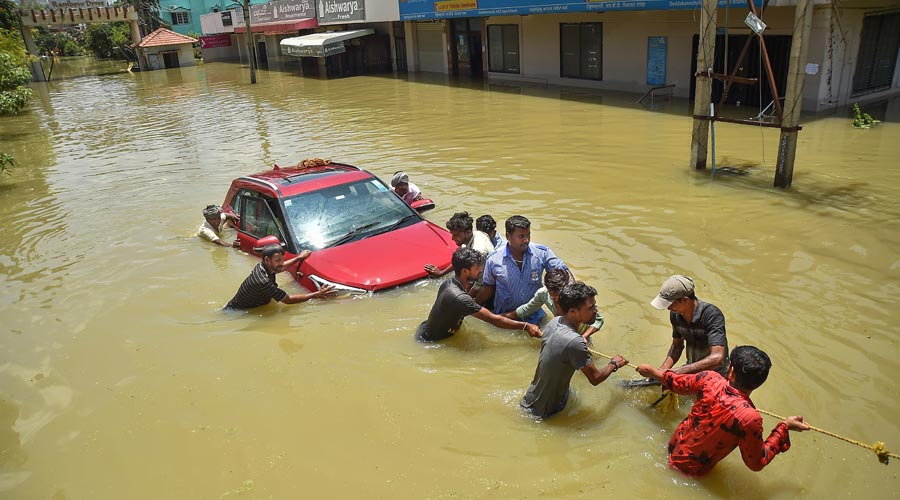 Rescuers try to pull out a car from flooded Rainbow Drive Layout after heavy monsoon rains at Sarjapur, in Bangalore