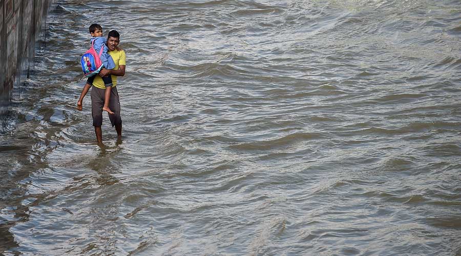 A man carrying his child wades through the waterlogged Outer Ring Road after heavy monsoon rains near Bellandur.