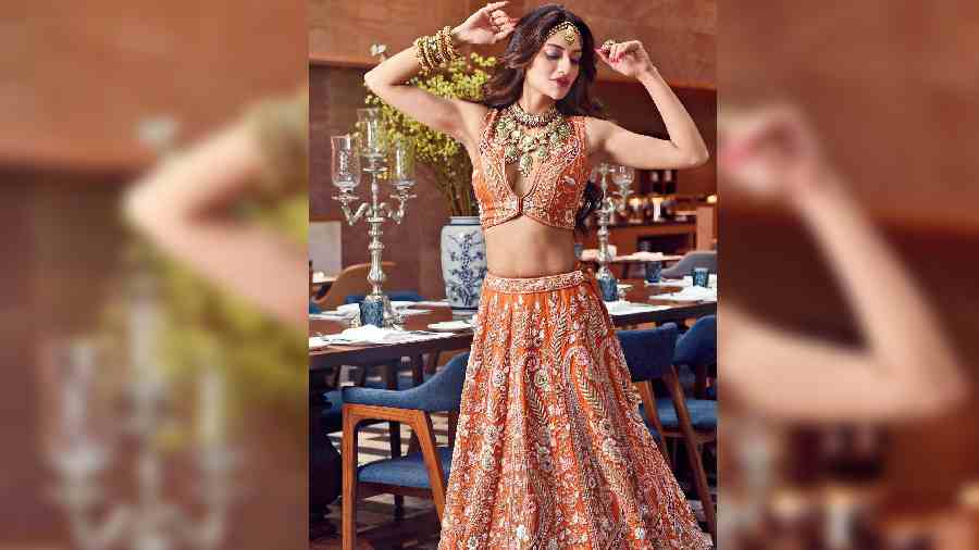 For the modern bride who’s not afraid of bold cuts yet wants to tie her look to tradition, this sunset orange lehnga with intricate sequin, white pearls, blush-pink crystal embellishments and zardosi in silver and gold is perfect. This outfit is a work of art. Turn heads at your cocktail event by treating this as a skirt and crop top, or add the heavily embellished dupatta to create a wedding look. We’ve channelled boho-chic vibes by skipping the dupatta and going for a kundan sheesh patti, along with chunky bangles in polki and uncut diamonds and a stunning two-layered polki, emeralds and uncut diamond necklace. The open wavy tresses and elegant make-up complete the look.