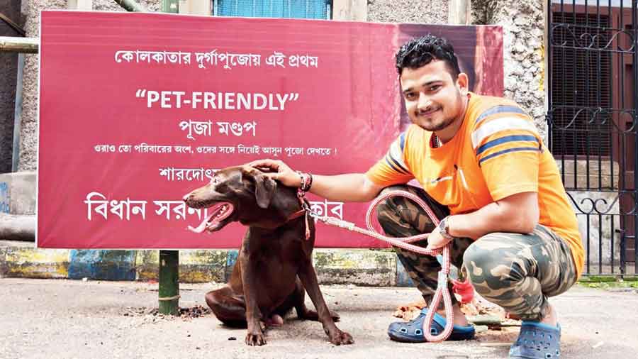A puja volunteer and his Labrador, posing before the banner 