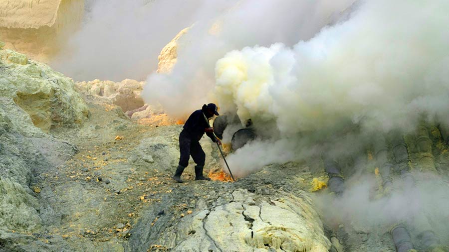 A miner breaks off sulphur chunks with his shovel as smoke jets out of the openings on the steaming slopes