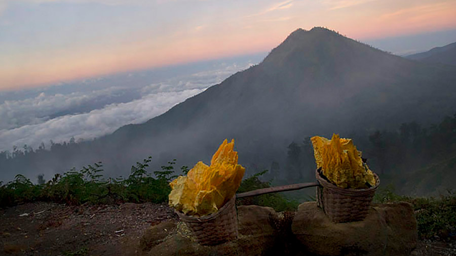 A pair of baskets containing extracted sulphur sit on a stony ledge, as dawn breaks over the mountain slopes 