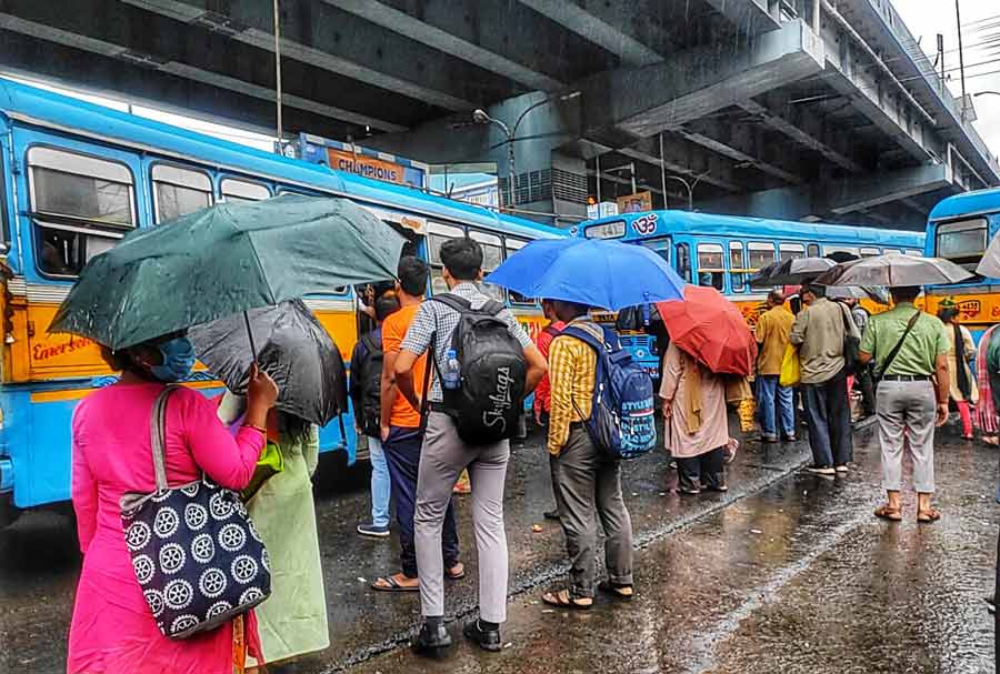 Office-goers, armed with umbrellas, wait at the bus stand near the VIP Road-Baguiati crossing.  