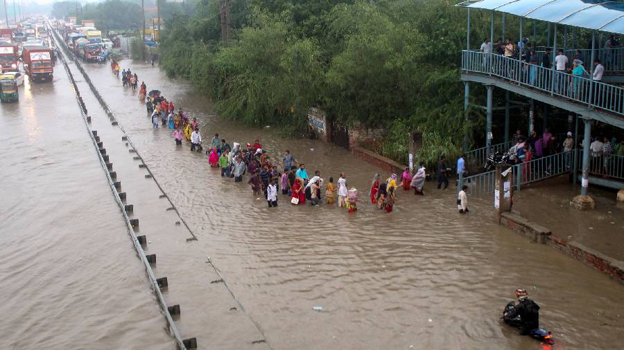 Commuters wade through the waterlogged Delhi-Gurugram Expressway service road after rainfall, in Gurugram