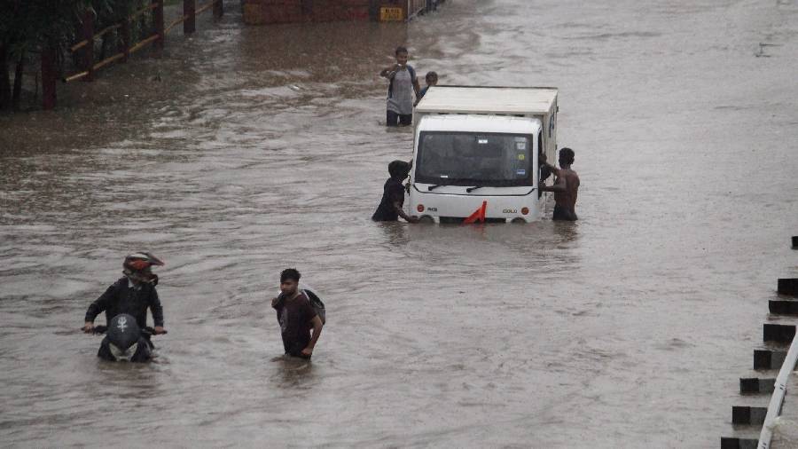 Commuters in Delhi push their vehicle down a waterlogged road