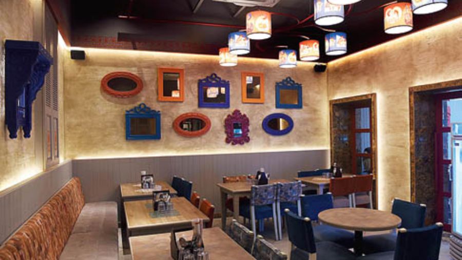 The space is done up in muted and earthy tones with royal blue velvet chairs adding colour. Vibrant lamps with Punjabi motifs, hang from the ceiling, and mirrors in different shapes and coloured frames line the walls. The outdoor area wears the same quirky and colourful vibe.