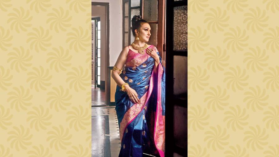 The dual bright shades of rani pink and midnight blue are perfect for the Navami night out look in this katan silk Benarasi sari. The classic pulled-up bun, complemented with the contemporary choice of minimal make-up in natural shades and statement jewellery pieces complete the look.