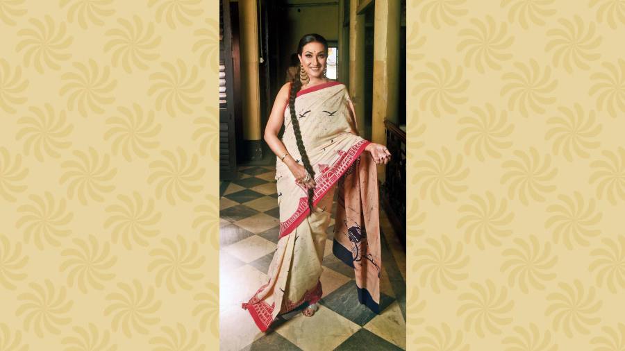 The quintessential red-and-white Dashami look, depicting the Kolkata skyline running along the border of the handmade cotton batik sari, is complemented with a classic touch in the hair and make-up. Simple nude make-up, the bindi, the hair tied in a long plait and the contemporary-favourite cascading chaandbalis complete the look.