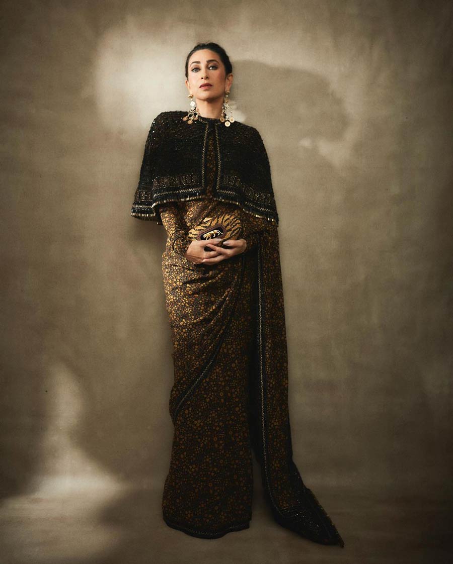 Karisma Kapoor stunned in a dark floral Sabyasachi sari with an embellished cape, a Sabyasachi clutch and tiered earrings. 