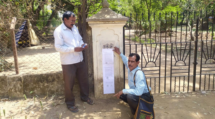 Visva-Bharati employees paste a three-page order on one of the pillars of the gate of Pratichi on Friday.