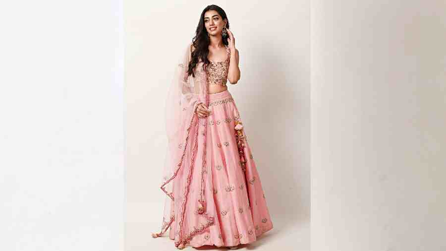 This dreamy lehnga in powder pink is handcrafted with intricategold reshamwork, elevated beautifully with a scalloped organza dupatta. Finished with fuchsia pink edging that makes it ideal for any modern-day bride or bridesmaid for a day function.
