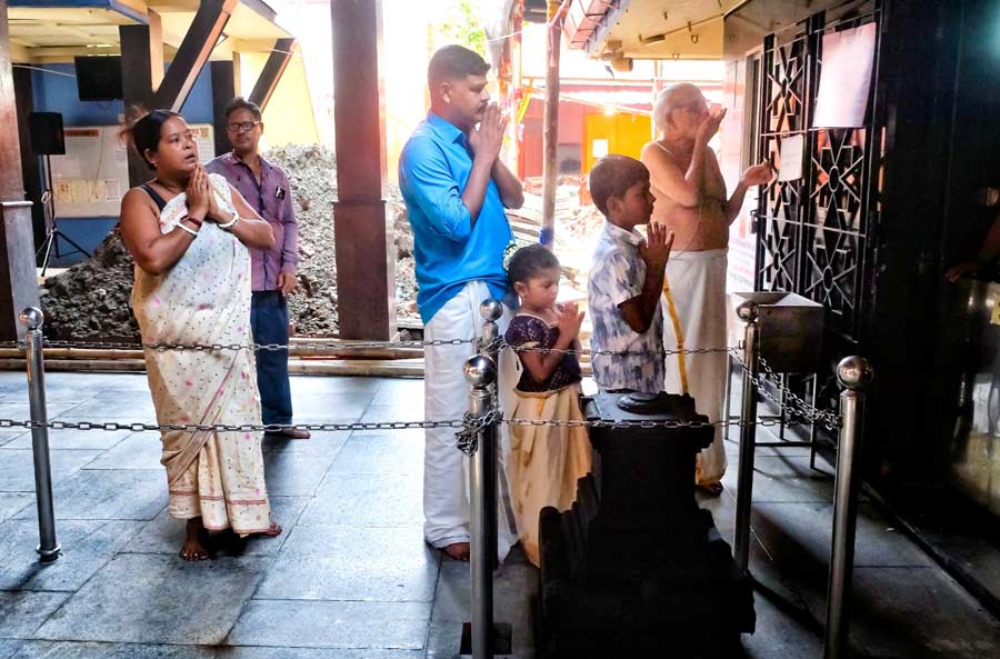 A devotee prays with his family members during aarti in traditional outfits at Sree Guruvayurappan Temple