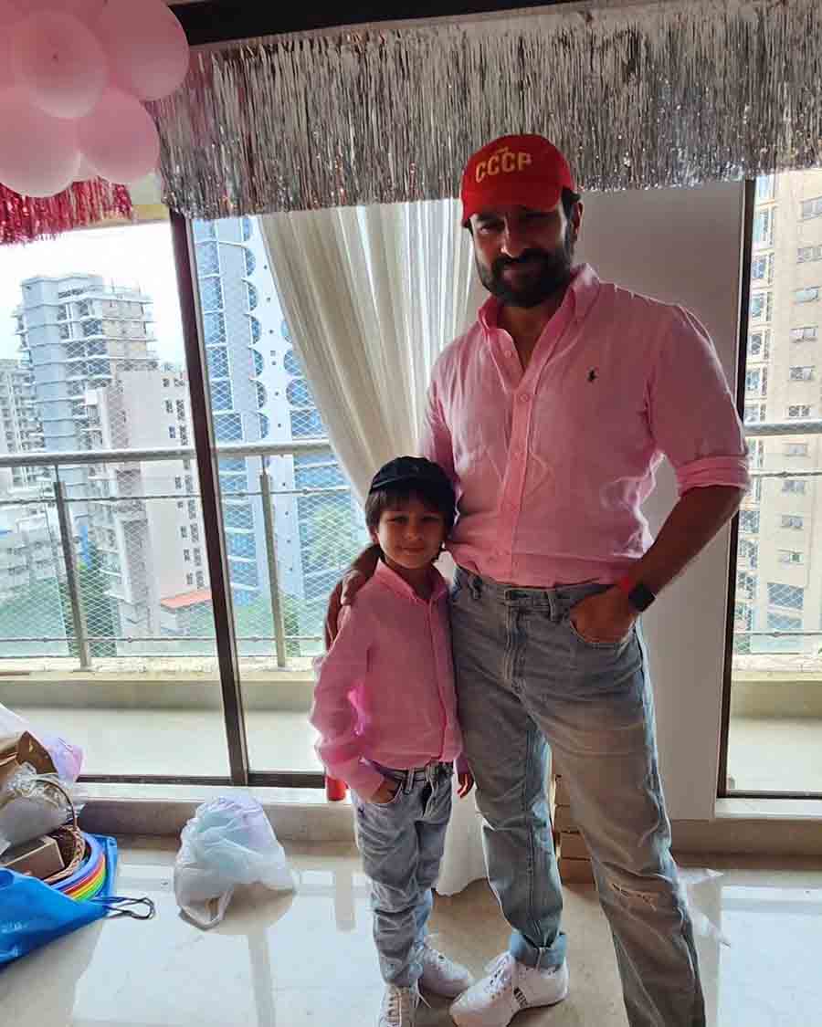 The father-son duo posed against a backdrop of silver streamers and pink balloons in matching shirts.