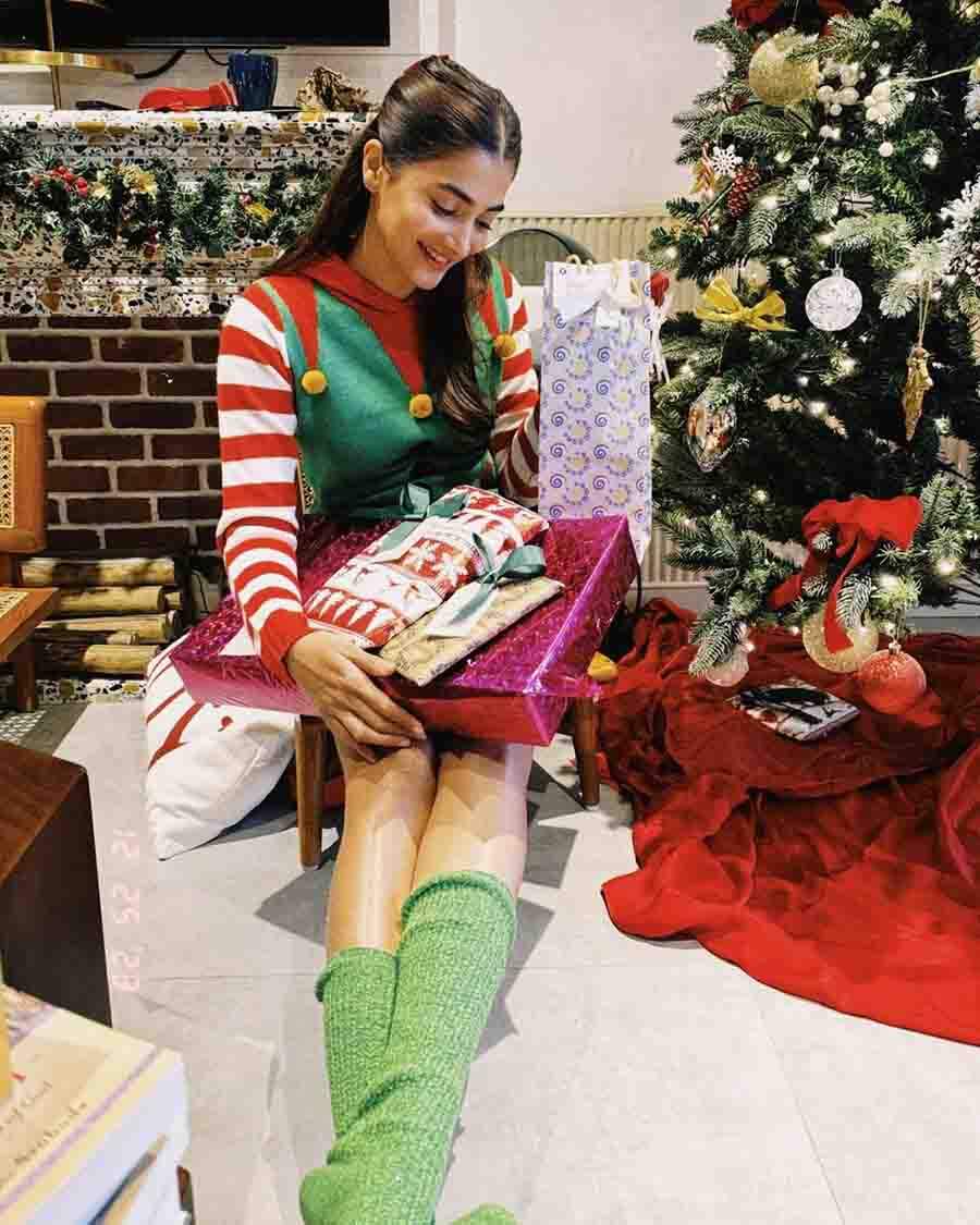 Pooja Hegde, in a holiday-themed jacket, posed with a Christmas tree and several Christmas presents on her lap.