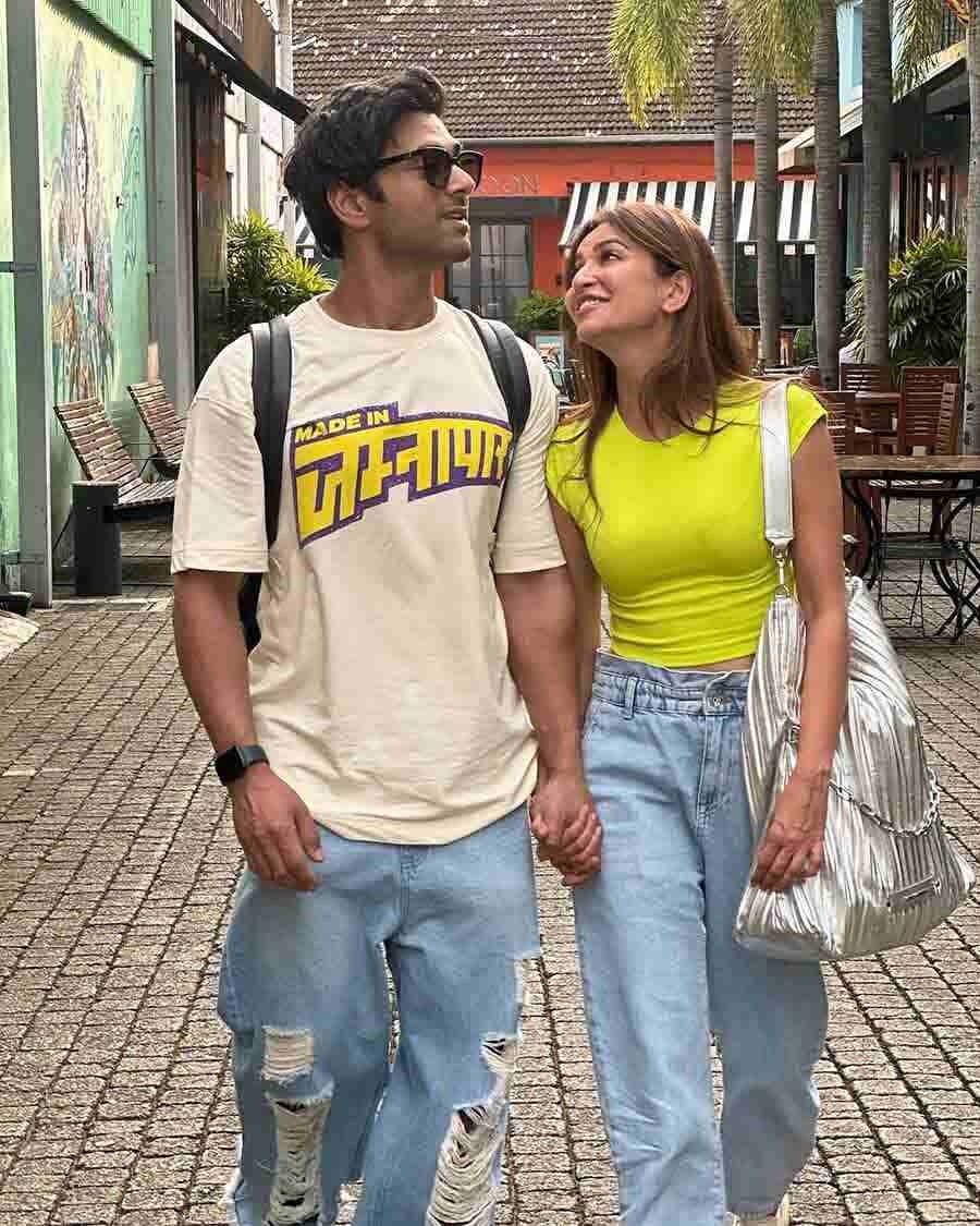 The couple hold hands and stroll across a city in casual outfits – funky tees paired with jeans. 