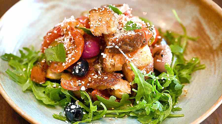 Insalata Panzanella: A fresh and vibrant plate, this salad brings together toasted bread, roasted tomatoes, baby onions, jalapenos, rocket leaves, amaranth pops, in a red winebased dressing.