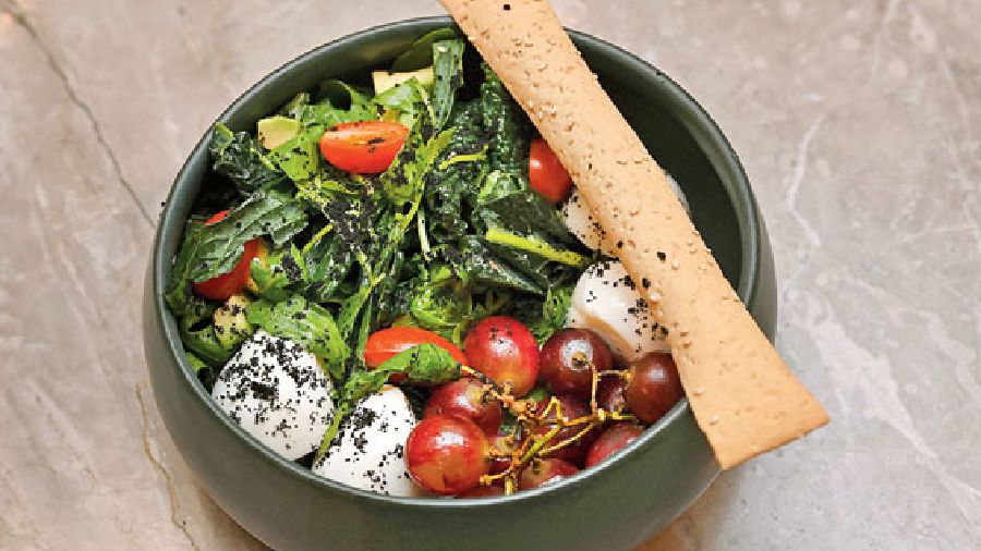 Bocconcini, California Grapes and Avocado Herb Vinaigrette: Cherry tomatoes, kale, arugula, sweet chilli and oregano dressing come together in this fresh and healthy bowl. The salad is topped with pounded activated charcoal to enhance digestion.