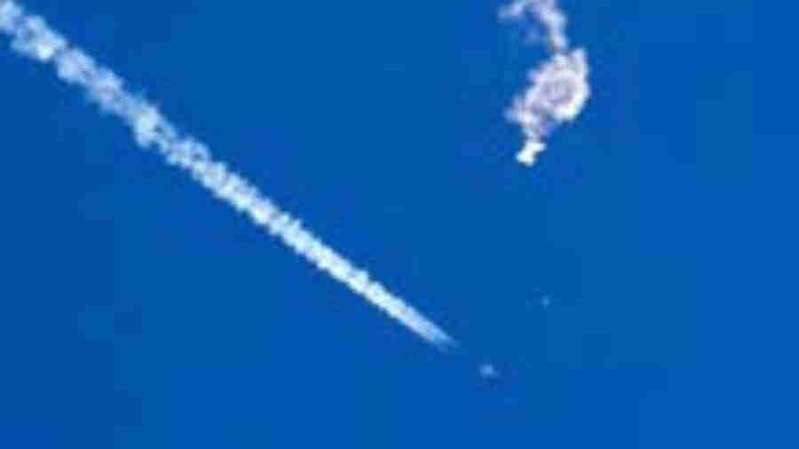 The remnants of the balloon drift above the Atlantic Ocean, just off the coast of South Carolina, with a fighter jet and its contrail seen below it. 