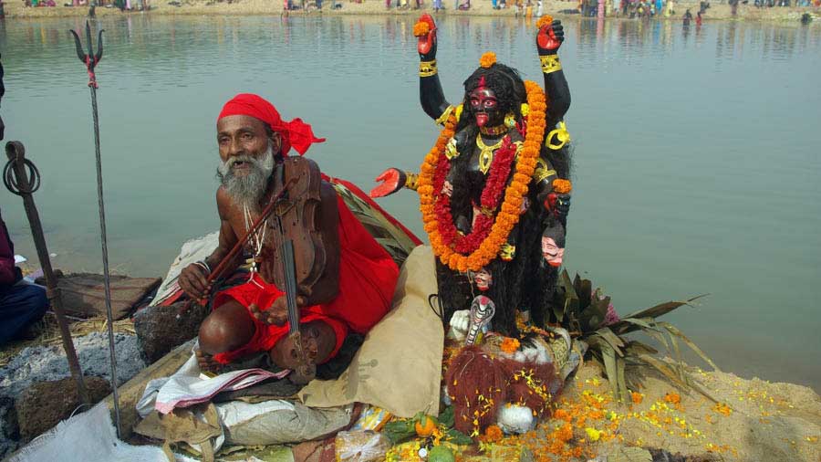 A sadhu playing a violin sitting besides the Ajay River