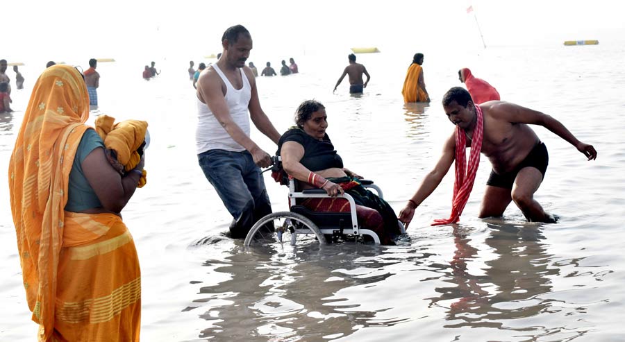 A man helps an elderly woman take a dip. Even as the auspicious timing to take the dip begins from 6.50pm on Saturday, countless braved the chilly weather and offered prayers at the Kapil Muni Ashram