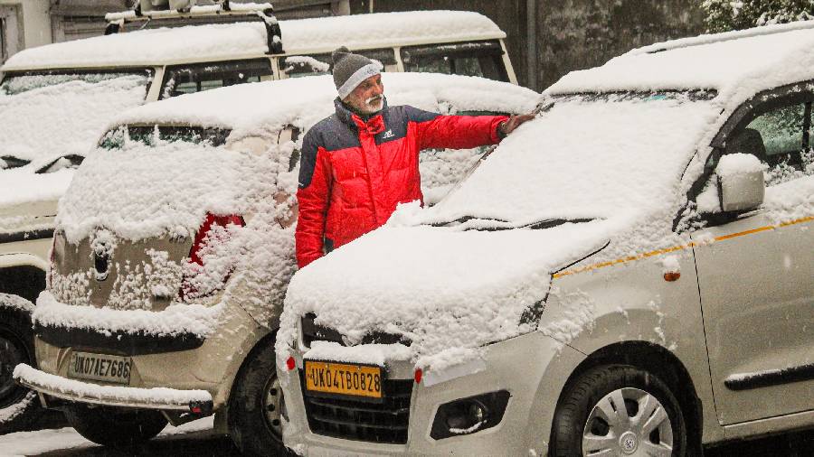A man clears snow from a car after heavy snowfall in Joshimath on Friday.
