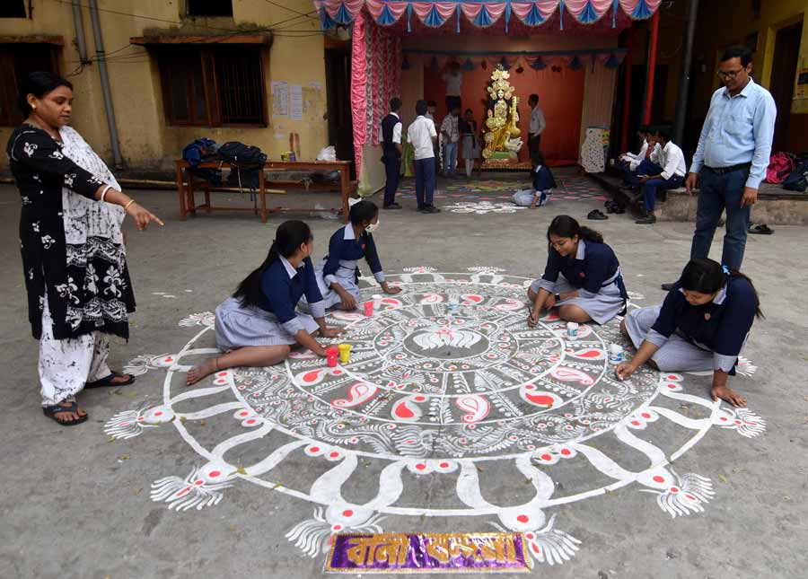 Students of Shyambazar A.V. school paint ‘alpona’ in front of the Saraswati Puja pandal