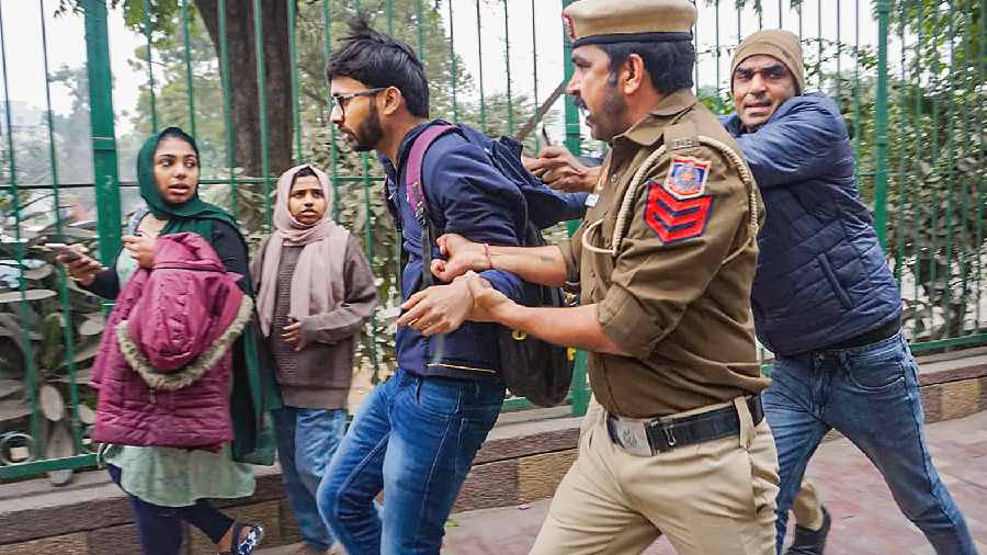 A cop detains a student on the Jamia Millia Islamia campus in New Delhi on Wednesday