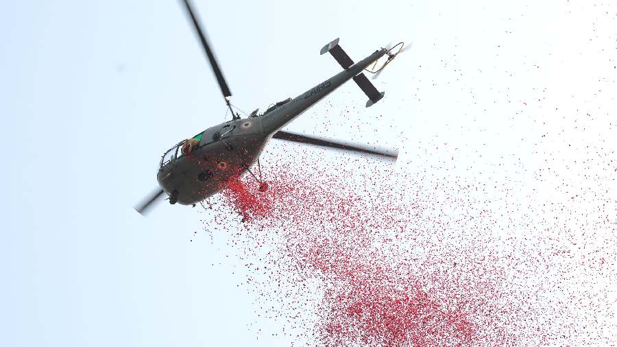 A helicopter hovers in the sky and showers rose petals. 