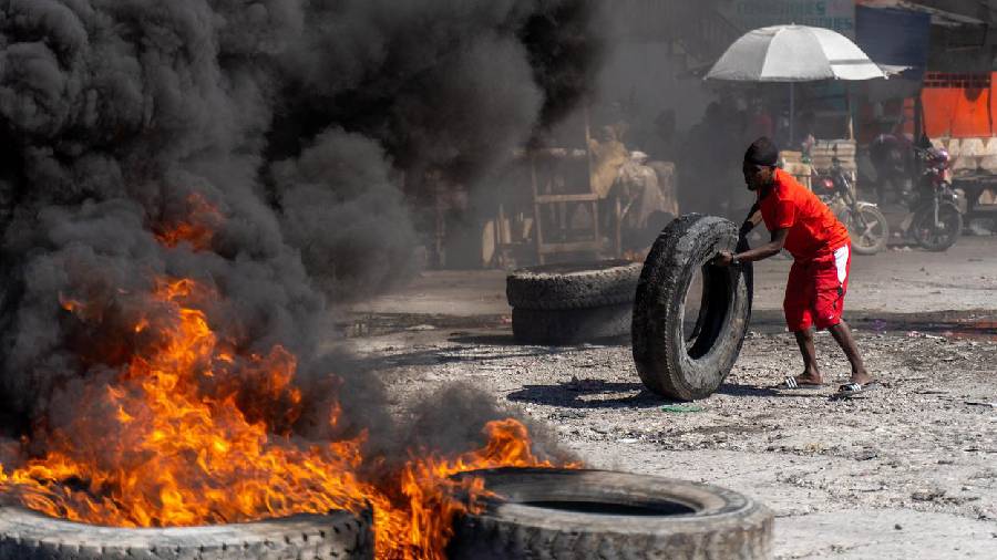 A man rolling a tire into a blockade of burning tires on the streets of Port-au-Prince 