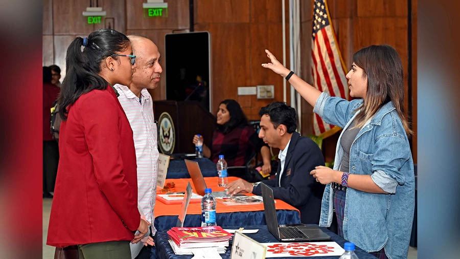 A parent and a school student interact with a representative of a university at the alumni fair