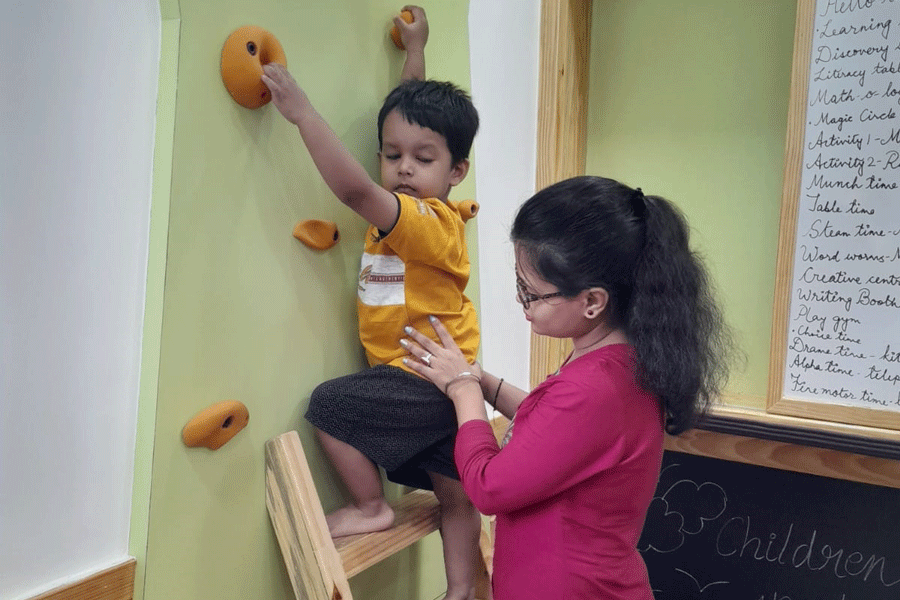 The child is assisted in climbing a wall in the classroom.