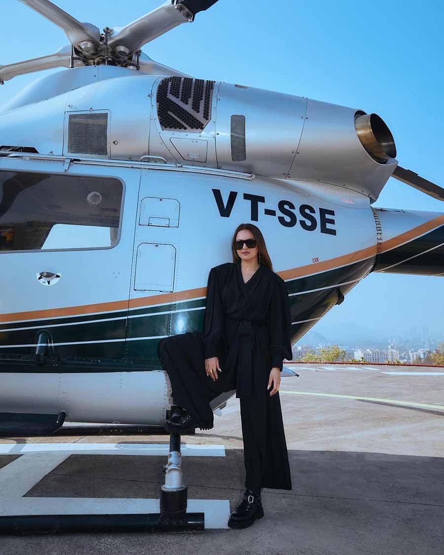Posing beside a helicopter, Sonakshi exudes girl boss energy in a stylish black blouse, high-waist trousers, boots and sunglasses. 