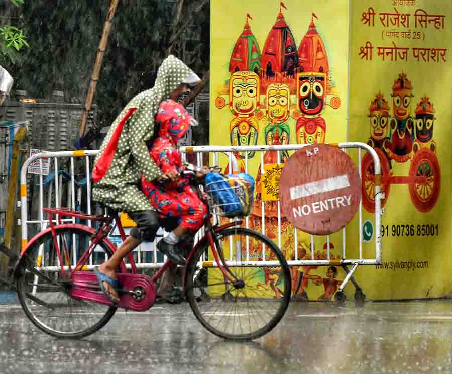 A cyclist escorts a school child to classes amid rain in north Kolkata 